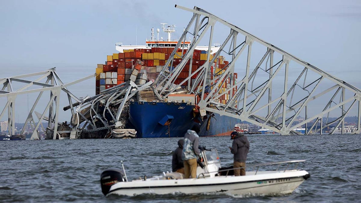 Cargo ship Dali is seen in the distance as rescuers work near by